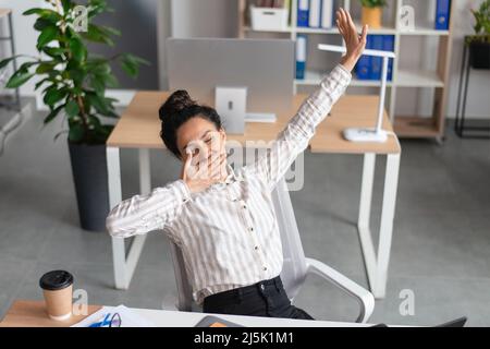 Müde junge Geschäftsfrau gähnend und streckend, müde von der Arbeit im Büro, müde am Arbeitsplatz, Platz kopieren Stockfoto