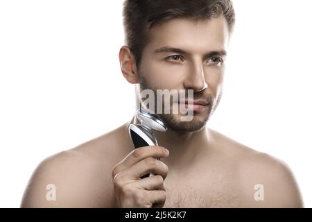 Der junge und gutaussehende Mann verwendet einen modernen Elektrorasierer auf weißem Hintergrund Stockfoto