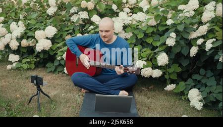 Mann mit Gitarre in Park Natur streamt online Podcast mit Gadgets Stockfoto
