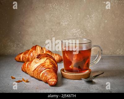 Frisch gebackene Croissants und Teetasse auf grauem Tisch Stockfoto