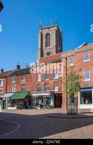 Fakenham Stadt, Blick im Sommer auf Geschäfte im Upper Market Place mit dem Turm der Pfarrkirche in der Ferne, Fakenham, Norfolk, Großbritannien Stockfoto