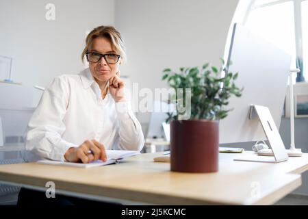 Ziemlich reife Geschäftsfrau, die im Büro sitzt Stockfoto