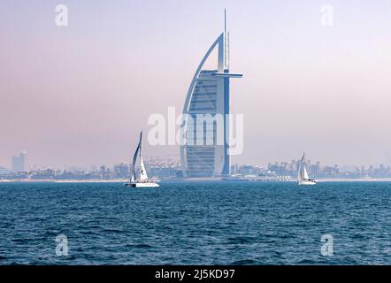 DUBAI, VEREINIGTE ARABISCHE EMIRATE - 9. APRIL: Segelboote fahren am 9. April 2022 vor dem Burj Al Arab Hotel am Jumeirah Beach in Dubai, Vereinigte Arabische Emirate. Die Stadt ist in den warmen Jahreszeiten oft von einer Mischung aus Wüstensand und Dampf bedeckt. Stockfoto