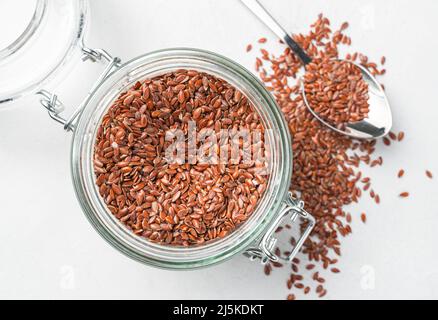 Leinsamen in einem transparenten Glas auf grauem Hintergrund. Draufsicht, Nahaufnahme. Stockfoto