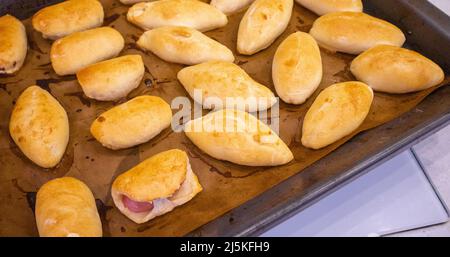 Legen Sie die frisch gebackenen Pasteten mit der Füllung auf ein mit Backpapier bedecktes Backblech. Köstliche frische hausgemachte Backwaren aus dem Ofen. Draufsicht. Stockfoto