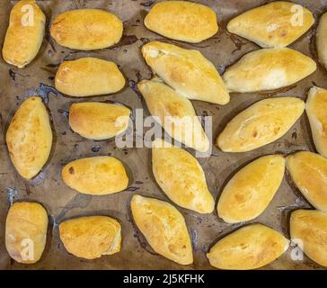 Legen Sie die frisch gebackenen Pasteten mit der Füllung auf ein mit Backpapier bedecktes Backblech. Köstliche frische hausgemachte Backwaren aus dem Ofen. Draufsicht Stockfoto