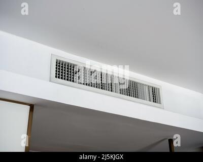 Klimaanlage, wandmontiertes Belüftungssystem an der Decke im weißen Hotelzimmer. An der Wand befindet sich ein Lüftungsgitter im Hotelzimmer. Stockfoto