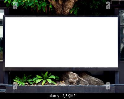 Weißer Leerraum auf einer Straßenplakatwand in der Nähe des großen Baumes und Gebäudes. Outdoor leeren horizontalen Rahmen Mockup auf der Straße für Werbung. Stockfoto