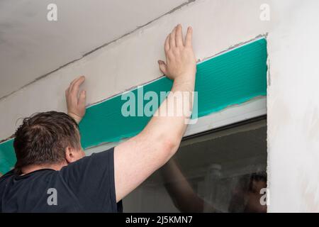 Der Master installiert Kunststoffabhänge an Fenstern aus isolierten Paneelen, die mit einer Schutzfolie abgedeckt sind. Reparatur eines Hauses oder einer Wohnung. Beenden mit Stockfoto