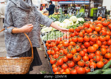 Kauf von frischem Bio-Gemüse auf dem Lebensmittelmarkt. Unkenntlich Mädchen mit Lebensmittelkorb Weidenkorb wählt reife Tomaten auf der Theke des Lebensmittelmarktes Stockfoto
