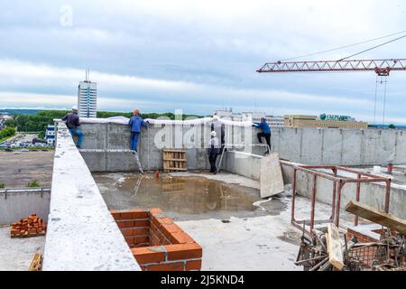 Kemerowo, Russland - 24. juni 2021. Auf dem Dach einer monolithischen Struktur montieren Arbeiter ein Einzäunungsgitter, um die Arbeiter vor fallenden Menschen und Stürzen zu schützen Stockfoto