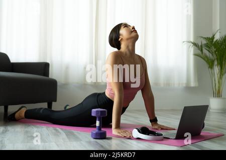 Fitnesstrainer mit virtuellen Yoga-Kurs mit Videoanruf auf Laptop. Remote Yoga Lehrer führt eine Lektion für Menschen Stockfoto