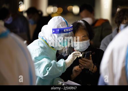 (220424) -- SHANGHAI, 24. April 2022 (Xinhua) -- Ein medizinischer Mitarbeiter hilft Huang Dongfang auf einem Smartphone in einem provisorischen Krankenhaus in Shanghai, Ostchina, am 23. April 2022. Huang Dongfang, die in einer dreieinhalb-stöckigen alten Wohnung im Wohngebiet Guangfu lebt, erholte sich von der COVID-19-Infektion und kehrte am Samstagabend nach Hause zurück. (Xinhua/Jin Liwang) Stockfoto