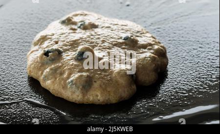Heidelbeer-Pfannkuchen auf einer gusseisernen Bratpfanne, bereit zum Umdrehen. Stockfoto