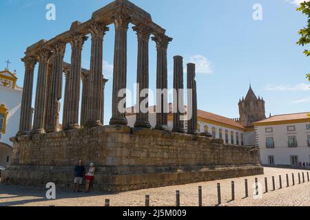 Ein touristisches Paar, das sich an den Überresten des römischen Tempels in Evora, Portugal, lehnt. Der Turm der Kathedrale im Hintergrund Stockfoto