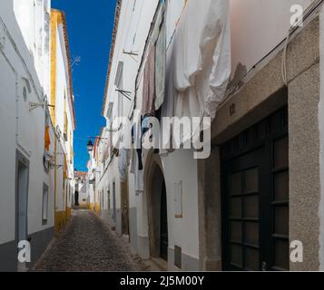 Trocknen von Wäsche in einer der malerischen Gassen mit Kopfsteinpflaster und weiß getünchten und gelben Häusern im historischen Zentrum von Evora, Portugal. Stockfoto