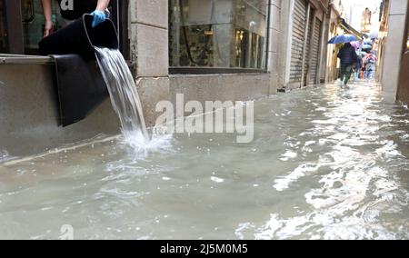 Entleeren des Wassers aus dem Laden mit einem Eimer während einer schrecklichen Flut auf der Insel venedig in italien Stockfoto