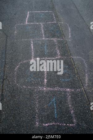 Die rosa-weiße Wachsmalstift-Zeichnung hopscotch auf der asphaltierten Straße Stockfoto