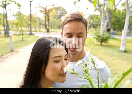 Multikulturelles Paar, das in einem Stadtpark tropische Blumen riecht Stockfoto