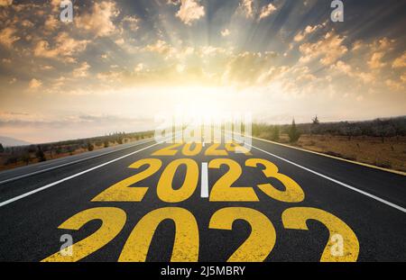 Das Wort 2023 auf der Autobahn Straße in der Mitte der leeren Asphaltstraße bei goldenem Sonnenaufgang geschrieben. Konzept für das neue Jahr 2023. Konzept der Planung und Herausforderung Stockfoto