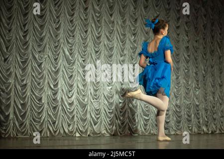 Ein Kind tanzt auf der Bühne. Performance eines Mädchens in einem blauen Kleid. Der Künstler zeigt Rock and Roll. Ein Kind in einer Tanzstunde. Stockfoto