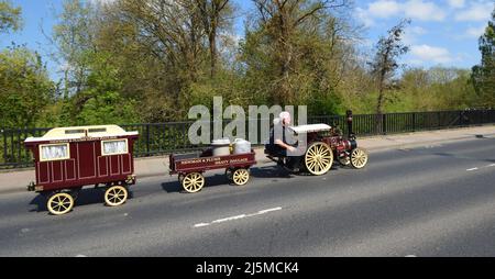 Miniatur-Dampflokomotive mit zwei Anhängern, die auf öffentlichen Straßen gefahren werden. Stockfoto