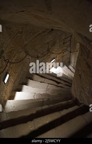 Eine steinerne Wendeltreppe aus dem Mittelalter, die in den Keller hinabführt, wo früher die Gefängniszellen waren.das Geländer ist einfach: Eine Kette Stockfoto