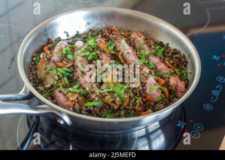 französische Chipolata-Spezialwürste, gekocht mit Linsen, Karotten und Petersilie Stockfoto