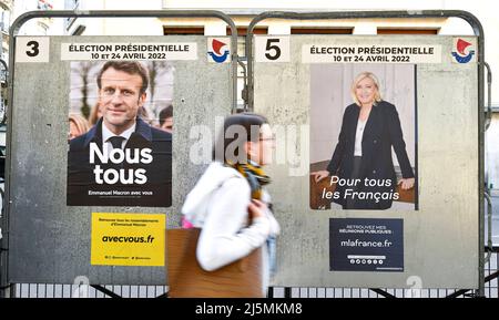 Paris, Frankreich. 24. April 2022. Ein Fußgänger übergibt offizielle Wahlkampfplakate auf einer Wahlplakatwand (Schild). Präsidentschaftsplakate auf ihren Wahlvorständen. Abbildung am 24. April 2022 in Paris, Frankreich. Die französischen Wähler kommen an die Wahlen, um für die zweite Runde der Präsidentschaftswahlen zu stimmen, um ihren neuen Präsidenten der Republik zwischen Emmanuel Macron (LREM) und Marine Le Pen (RN, 'Rassemblement National') zu wählen. Kredit: Victor Joly/Alamy Live Nachrichten Stockfoto