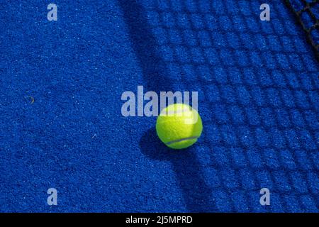 Ball im Schatten des Netzes eines blauen Paddle-Tennisplatzes. Stockfoto