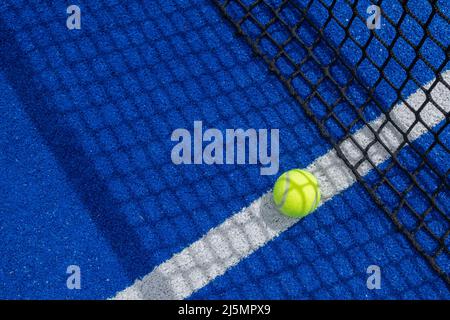 Ball im Schatten des Netzes eines blauen Paddle-Tennisplatzes. Stockfoto