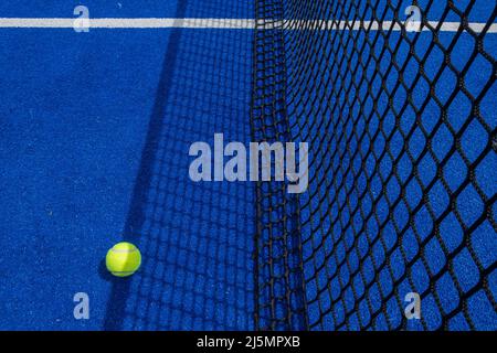 Ball im Schatten des Netzes eines blauen Paddle-Tennisplatzes. Stockfoto