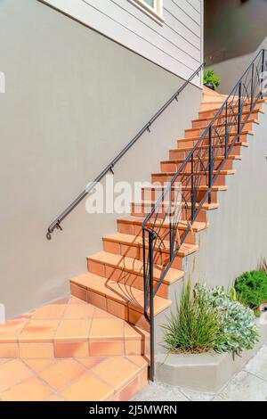 Außentreppe mit gefliesten Stufen und Eisengeländern in San Francisco, Kalifornien. Eingang eines Hauses mit grauem Äußeren und Pflanzen in der Nähe der Wand Stockfoto