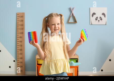 Glückliches kleines Mädchen hält verschiedene Pop es fidget Spielzeug im Kinderzimmer Stockfoto