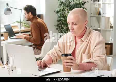 Inhalt junge kaukasische Geschäftsfrau im lässigen Outfit, die Kaffee trinkt und einen Laptop benutzt, während sie online arbeitet Stockfoto