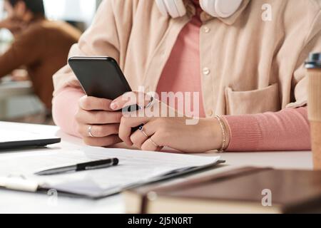 Nahaufnahme einer nicht erkennbaren Frau in Ringen, die am Schreibtisch sitzt und am Telefon Nachrichten abcheckt Stockfoto