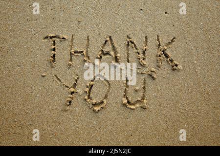 Danke – handschriftliche Inschrift auf dem weichen Strandsand. Stockfoto