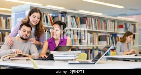 Drei Erwachsene Studenten arbeiten an einem Laptop und lesen Bücher in einer öffentlichen Bibliothek Stockfoto