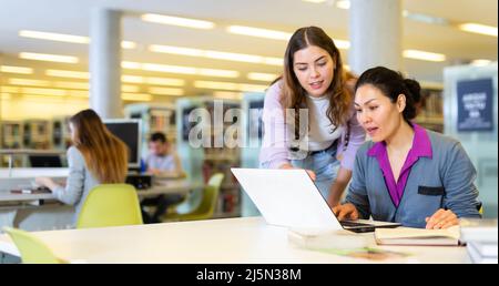 Zwei Wissenschaftlerinnen nutzen Bücher und Laptops für die Forschung in der Bibliothek Stockfoto
