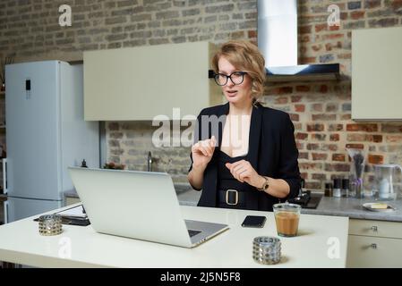 Ein Mädchen in einer Brille, das gestikuliert, während es in einem Videoanruf mit ihren Kollegen spricht. Stockfoto