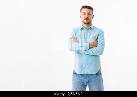 Porträt eines fröhlichen jungen Mannes in einem blauen Hemd auf weißem Hintergrund. Der Typ steht, schaut auf die Kamera und lächelt. Stockfoto