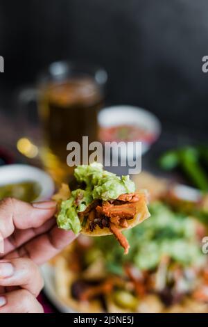 Hand hält mexikanische Nacho-Chips mit amerikanischem Käse und Avocado, traditionelles Essen in Mexiko Lateinamerika Stockfoto