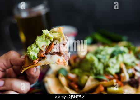 Hand hält mexikanische Nacho-Chips mit amerikanischem Käse und Avocado, traditionelles Essen in Mexiko Lateinamerika Stockfoto