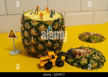 Mini-Bauleute arbeiten an einer Ananas. Schneiden und Schneiden. Stockfoto