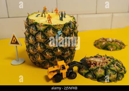 Mini-Bauleute arbeiten an einer Ananas. Schneiden und Schneiden. Stockfoto