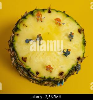 Mini-Bauleute arbeiten an einer Ananas. Schneiden und Schneiden. Stockfoto