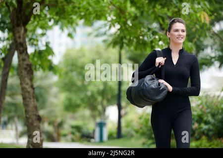 Aufgeregte junge Frau, die eine Sporttasche trägt, wenn sie morgens zum Yoga-Studio geht Stockfoto