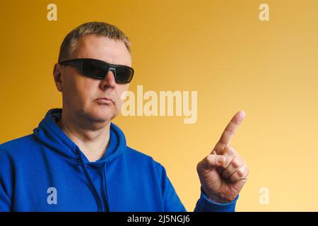 Porträt eines Mannes mit blauem Hoodie und Sonnenbrille. Der Europäer zeigt mit dem Finger Stockfoto