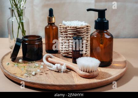 Kosmetikflaschen, Gesichtsbürste und Ohrstöcke auf Holztablett. Spa und Wellness, Zero Waste Konzept. Stockfoto