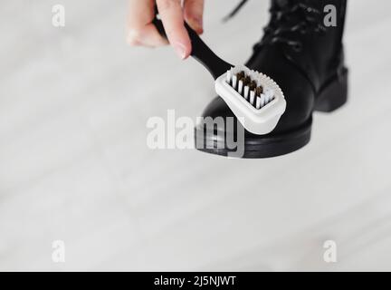 Damenhände wischen einen Lacklederstiefel von Schmutzstaub ab. Pflege von Lacklederschuhen.Schutz von Schuhen bei regnerischem, nassem Wetter. Stockfoto